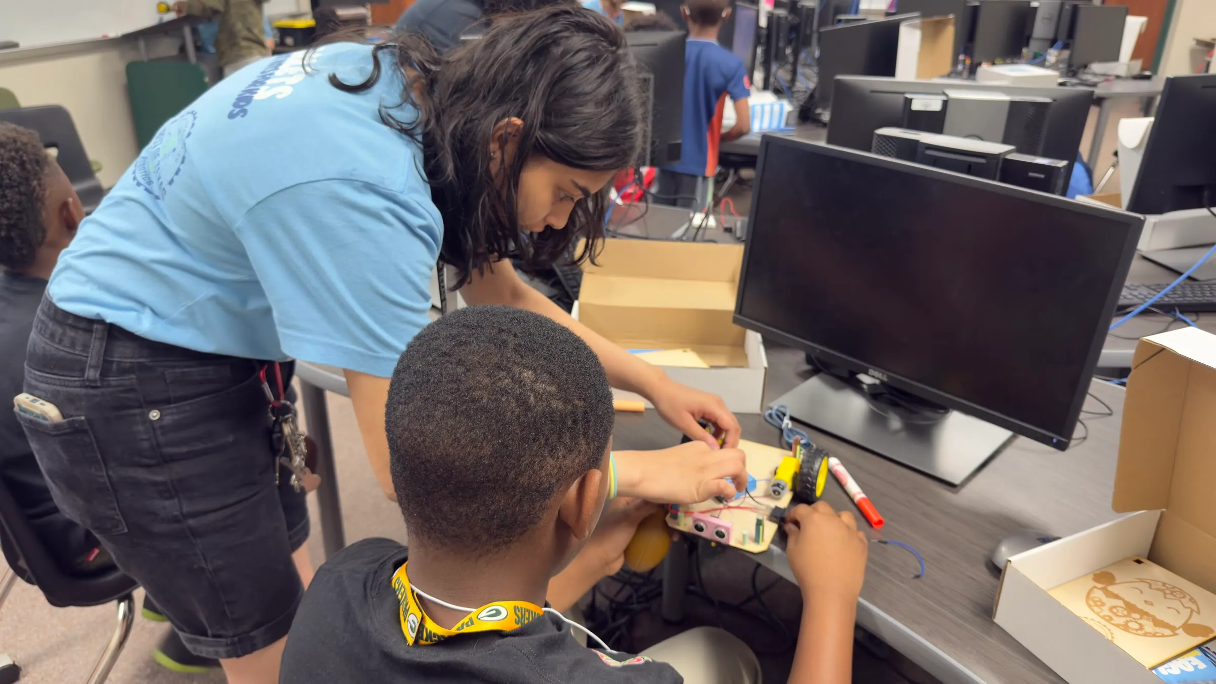 An Eaglets student instructor helps a younger student connect components on a robot kit.