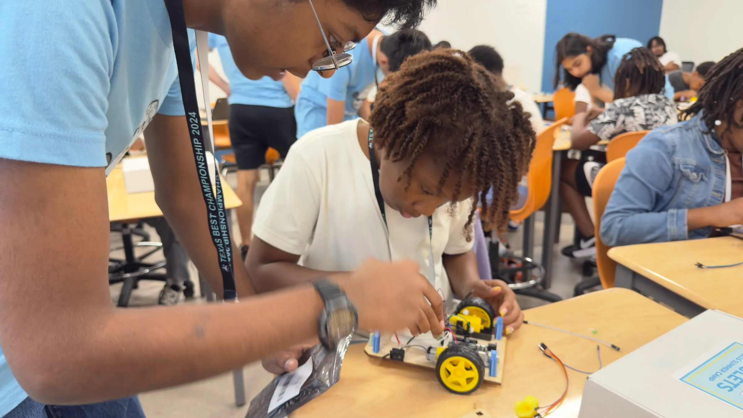 An Eaglets instructor guides a student while she works on a wheeled robot.
