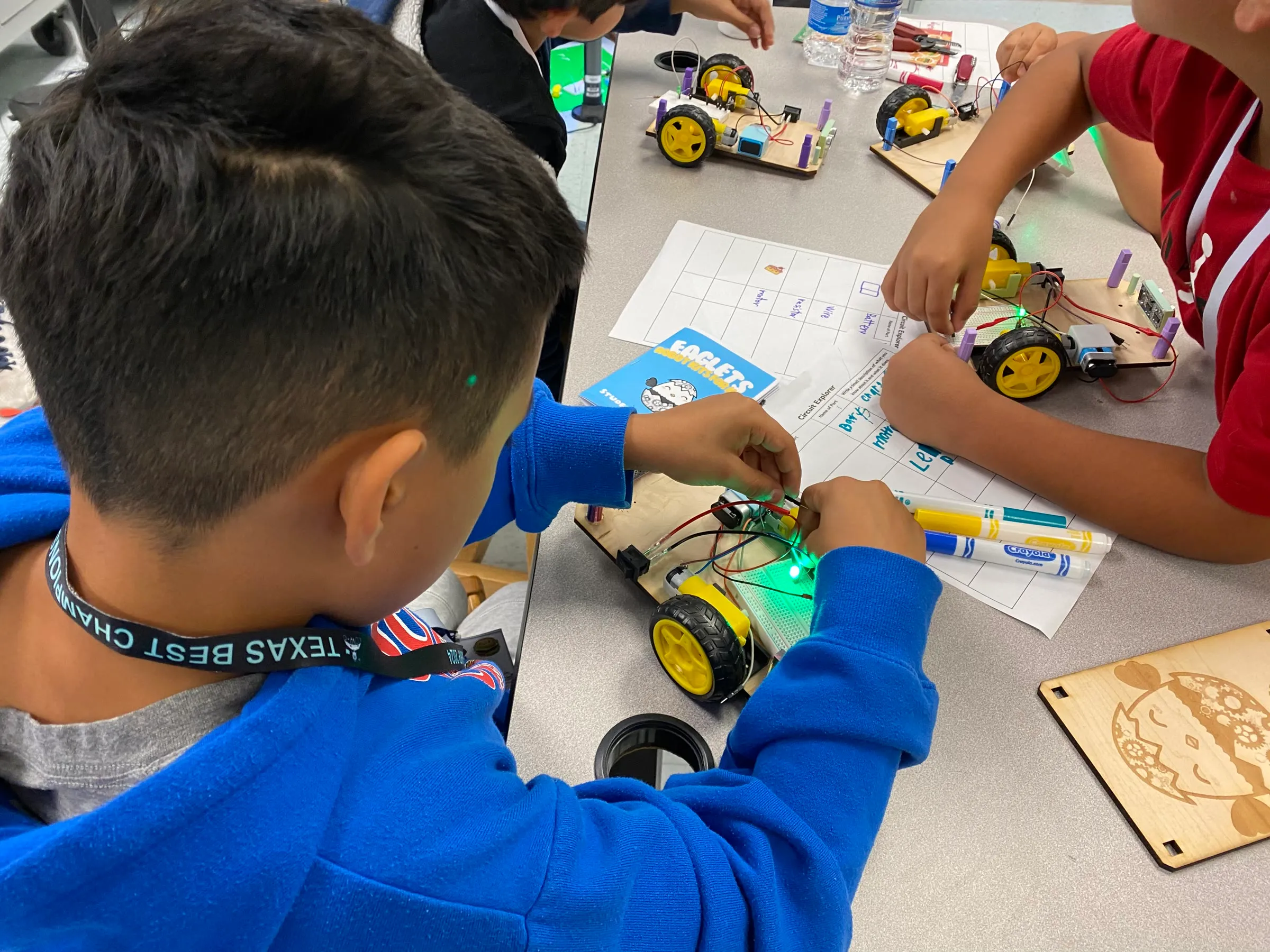 Students work together around a wired robot kit during a hands-on robotics activity.