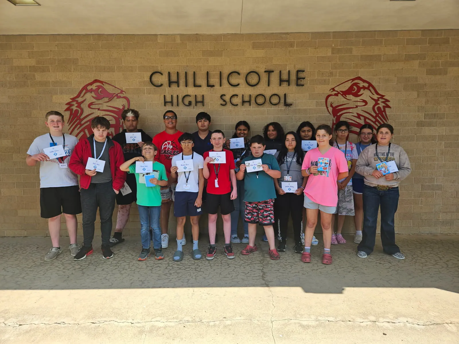 Camp Code participants and instructors hold certificates outside a school building.