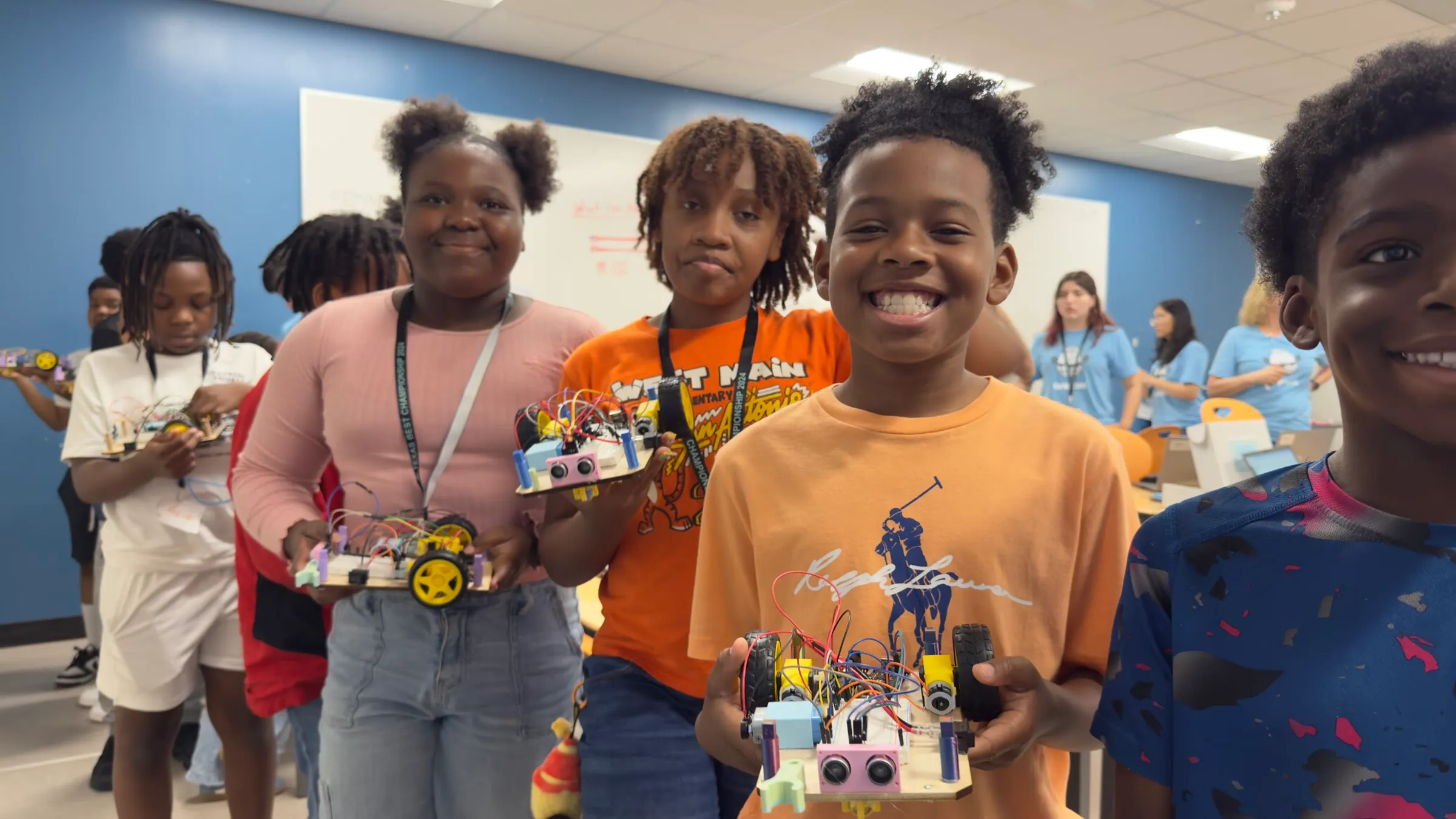 Students smile and hold the working robots they built during a robotics camp.