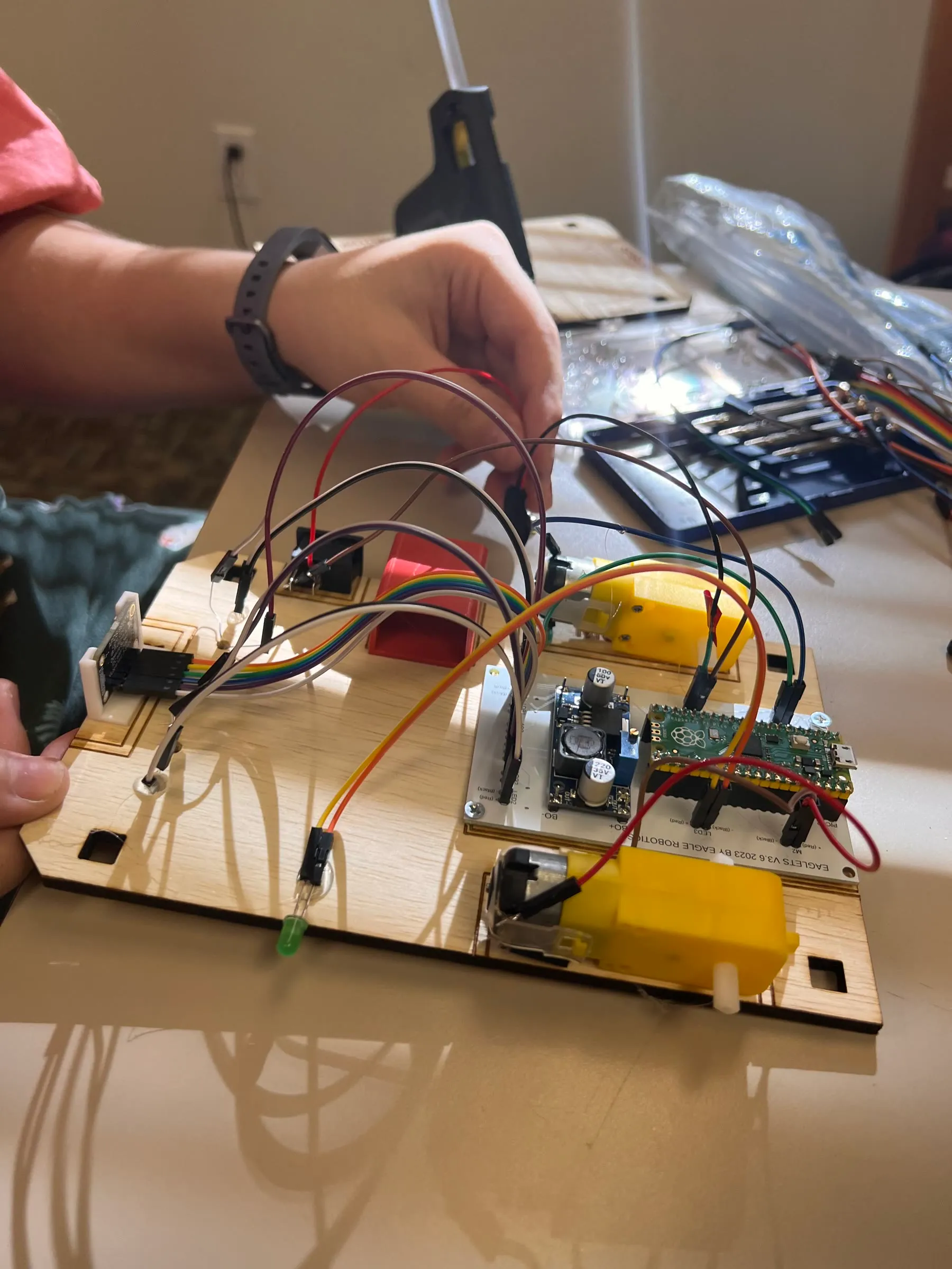 Close-up of hands assembling an Eaglets robot, with motors, wiring, and a microcontroller visible.