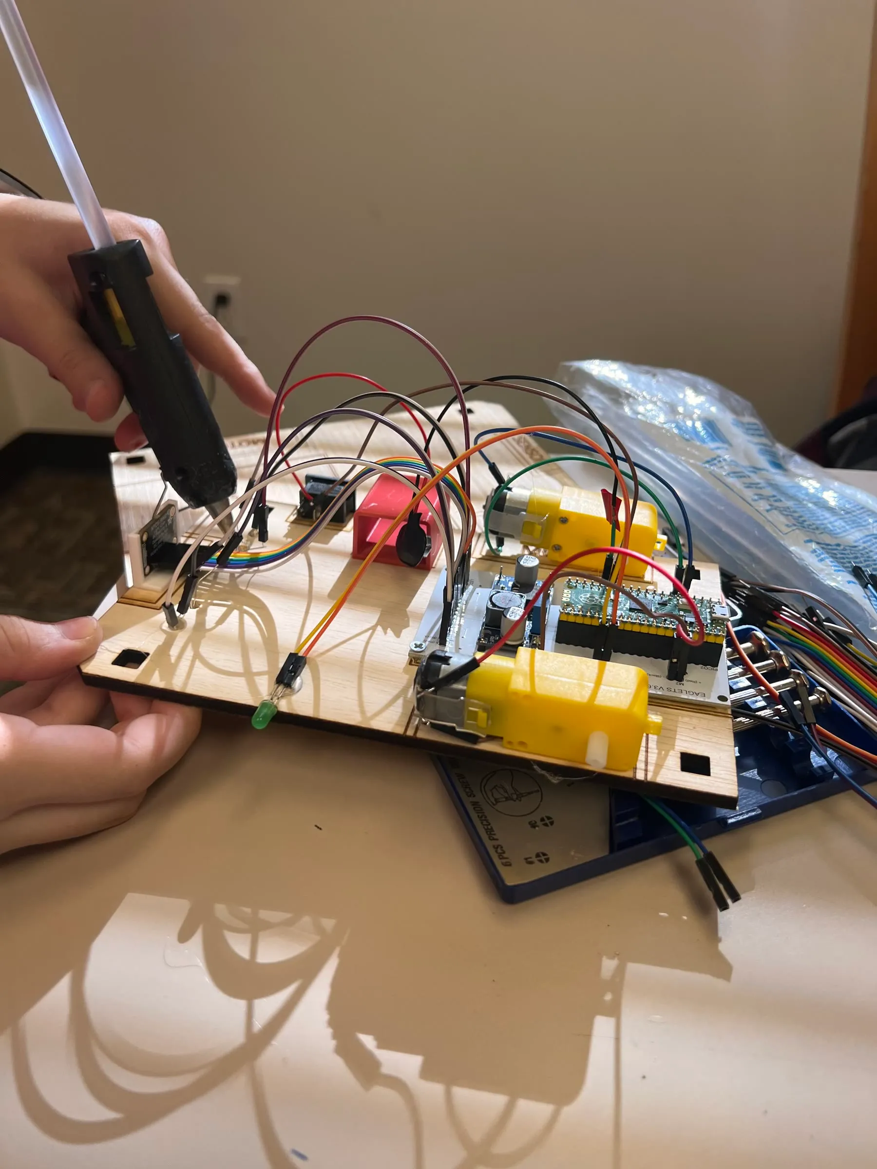 Hands using a glue tool while assembling wiring and components on an Eaglets robot chassis.