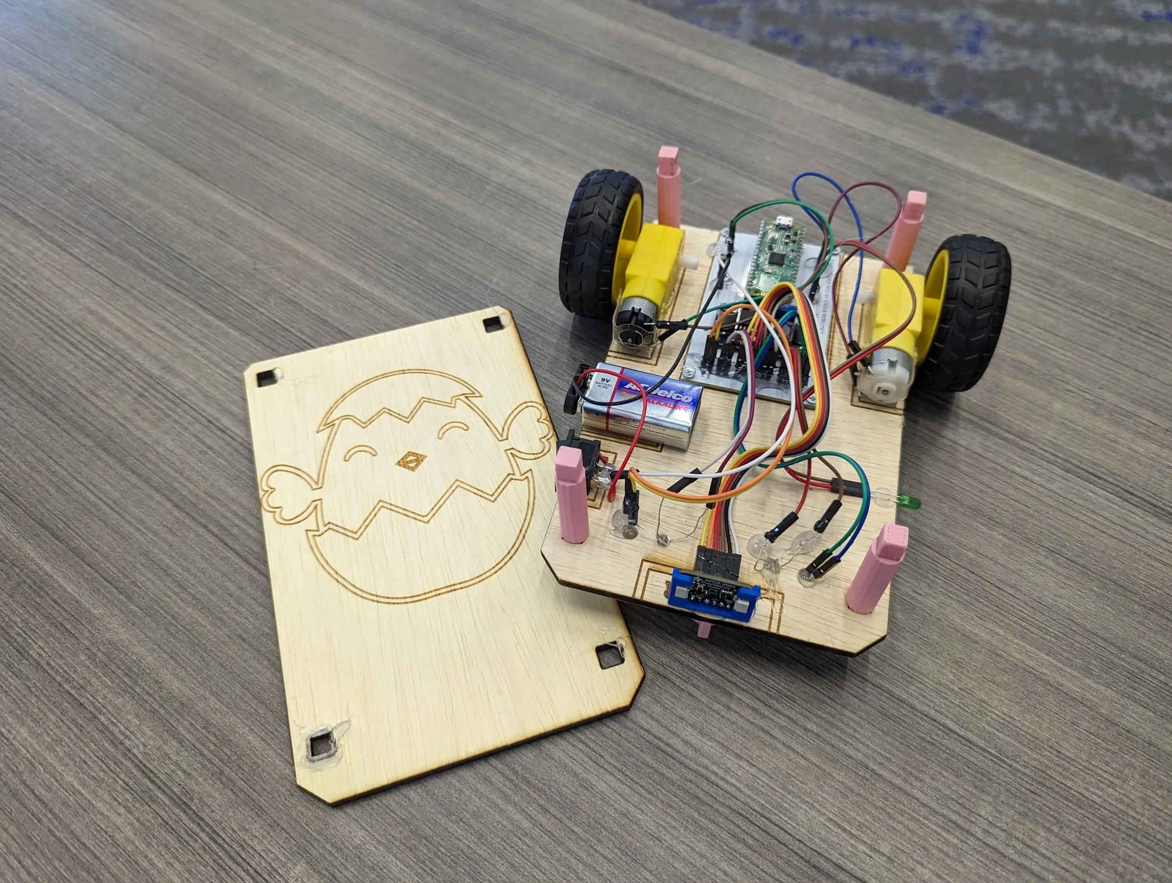 An Eaglets robot kit with its engraved wooden lid beside the open chassis, showing the wheels, motors, controller, battery, and wiring.