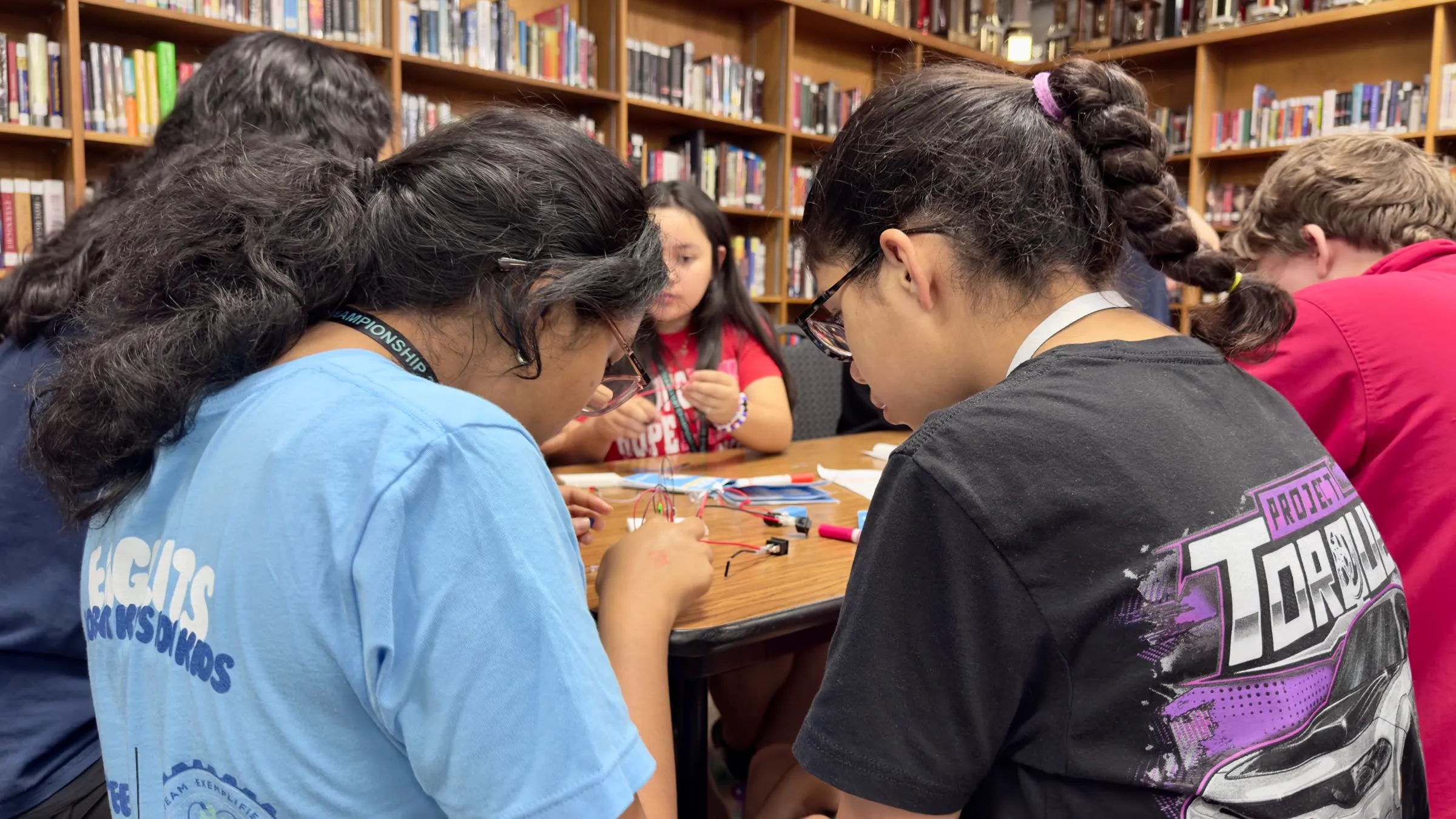 Students work together on wiring and electronics at a library table.